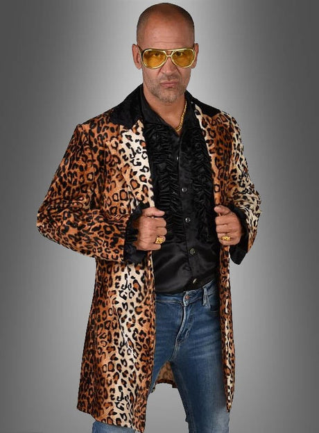 Ein kahlköpfiger Mann mit einer gelb getönten Sonnenbrille, dem „Pimp Mantel Leo Herrenkostüm“ – einem Mantel mit Leopardenmuster – sowie einem schwarzen Rüschenhemd und Jeans steht vor einem grauen Hintergrund mit Farbverlauf.