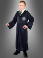 Ein Kind, das eine Slytherin-Schuluniform trägt – darunter die Slytherin-Robe von Draco Malfoy aus „Harry Potter“, ein weißes Hemd, eine gestreifte Krawatte und schwarze Schuhe –, steht vor einem schlichten grauen Hintergrund.