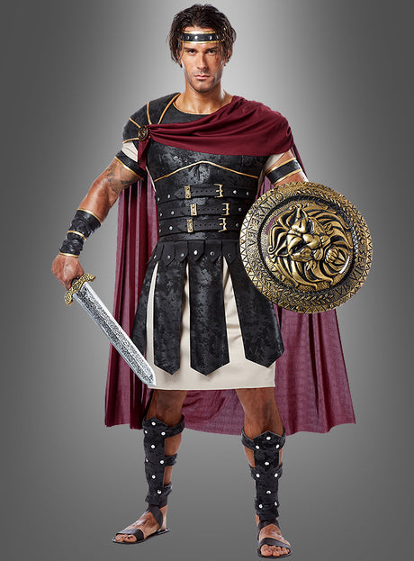Ein Mann, gekleidet wie ein römischer Gladiator, trägt das Römer-Kostüm „Gladiator Flavus“ mit einer markanten schwarzen Rüstung, einem wallenden roten Umhang und Ledersandalen. Er steht vor einem grauen Hintergrund und hält in der rechten Hand ein Schwert und in der linken einen verzierten Schild.