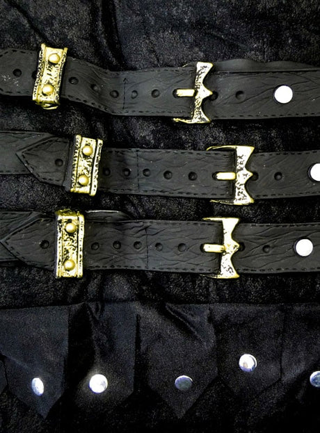Drei schwarze Ledergürtel mit verzierten goldenen Schnallen, die an das Römer-Kostüm „Gladiator Flavus“ erinnern, liegen parallel auf einem schwarzen Stoffhintergrund, wobei am unteren Bildrand silberne Nieten zu sehen sind.