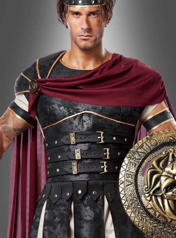 Ein Mann im Römer-Kostüm „Gladiator Flavus“, bestehend aus einem burgunderroten Umhang, einer schwarzen Rüstung mit goldenen Verzierungen und einem runden Schild, das mit einem Löwenkopf verziert ist.