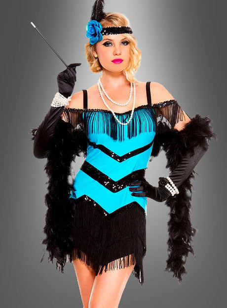 Eine Person, die das Flapperkleid mit Zubehör trägt – darunter ein blau-schwarzes Fransenkleid, lange schwarze Handschuhe, ein Feder-Stirnband, Perlenketten und eine Zigarettenspitze –, steht vor einem grauen Hintergrund; ein ideales 20er-Jahre-Kostüm für jedes Mottoparty-Outfit.