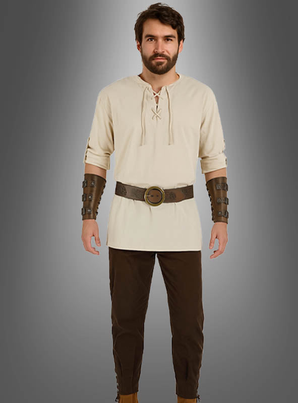 Ein Mann steht mit dem Blick nach vorne, gekleidet in das 5-teilige Mittelalter-Kostüm-Set für Herren – bestehend aus einer beigen Tunika, einer braunen Hose, einem breiten Gürtel und braunen Armschienen –, vor einem grauen Hintergrund mit Farbverlauf.