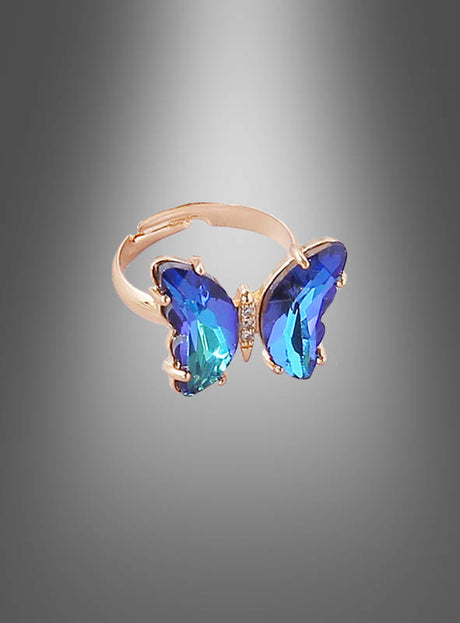 Wir präsentieren den verstellbaren Schmetterling-Ring aus Glas: ein goldener Ring mit Schmetterlingsmotiv, dessen Flügel aus blauen und türkisfarbenen Glassteinen sich vor einem grauen Farbverlauf abheben. Dieses elegante Stück Glas-Schmetterlingsschmuck ist größenverstellbar und somit eine vielseitige und auffällige Ergänzung für jede Damen-Modeschmuckkollektion.