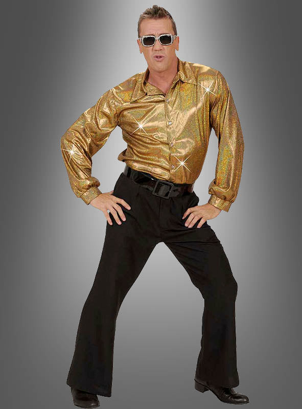 Ein Mann mit Sonnenbrille, dem goldenen „Glitzer Hemd Herren“ und einer schwarzen Schlaghose posiert mit den Händen in den Hüften vor einem grauen Hintergrund mit Farbverlauf – und verkörpert damit die Essenz eines coolen Outfits im Stil der 70er Jahre.