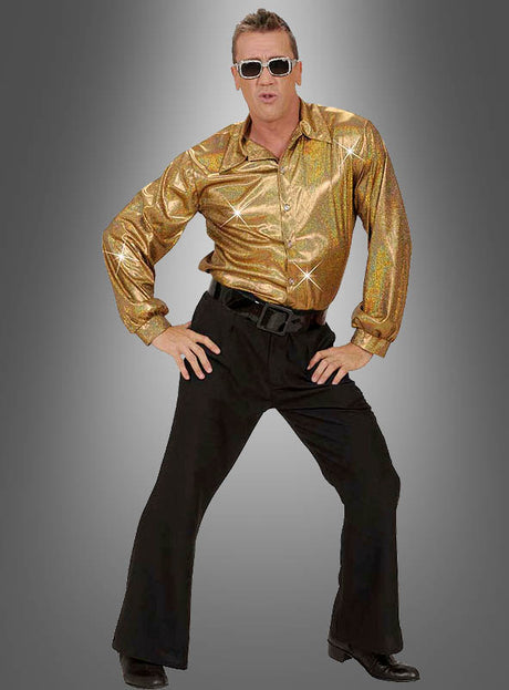 Ein Mann mit Sonnenbrille, dem goldenen „Glitzer Hemd Herren“ und einer schwarzen Schlaghose posiert mit den Händen in den Hüften vor einem grauen Hintergrund mit Farbverlauf – und verkörpert damit die Essenz eines coolen Outfits im Stil der 70er Jahre.