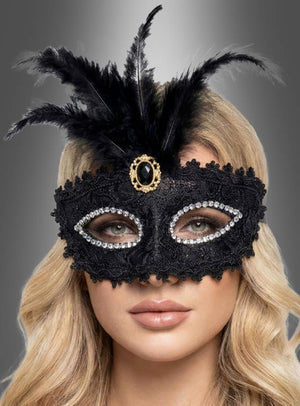 Eine Person mit langen blonden Haaren trägt die „Maskenball“-Augenmaske mit Spitze in Silber oder Schwarz, verziert mit Federn und Strasssteinen, vor einem grauen Hintergrund mit Farbverlauf.