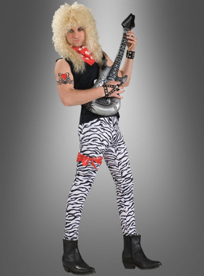 Eine Person mit einer blonden Perücke, einer Hose mit Zebradruck, schwarzen Stiefeln und einem roten Schal, die eine aufblasbare Gitarre in der Hand hält und vor einem grauen Hintergrund steht.