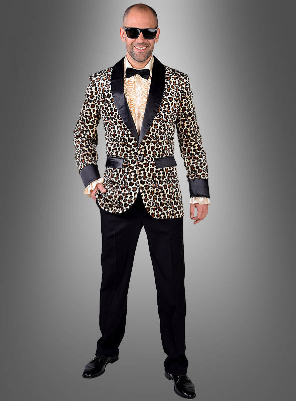 Ein Mann mit Sonnenbrille, einer „Leoprint Jackett Deluxe“ mit schwarzem Revers, Fliege, Hemd und schwarzer Hose steht lächelnd vor einem grauen Hintergrund mit Farbverlauf.