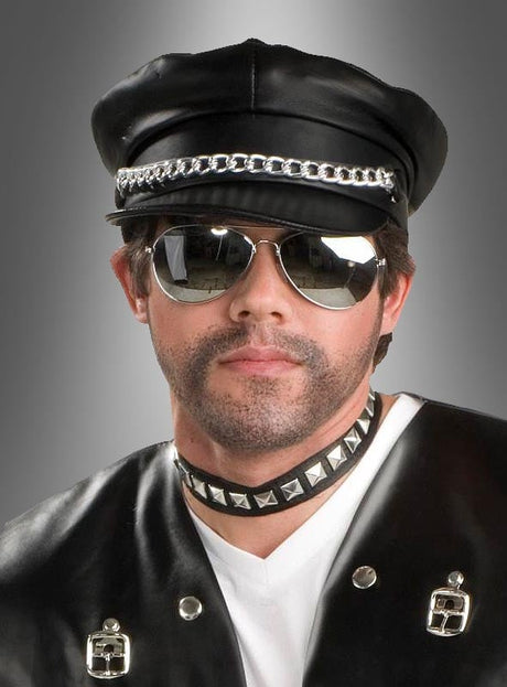 Ein Mann, der die „Rocker-Mütze schwarz im Lederlook“, eine Pilotenbrille, ein mit Nieten besetztes Halsband und eine schwarze Lederweste mit Metallakzenten trug, posierte vor einem grauen Hintergrund mit Farbverlauf.