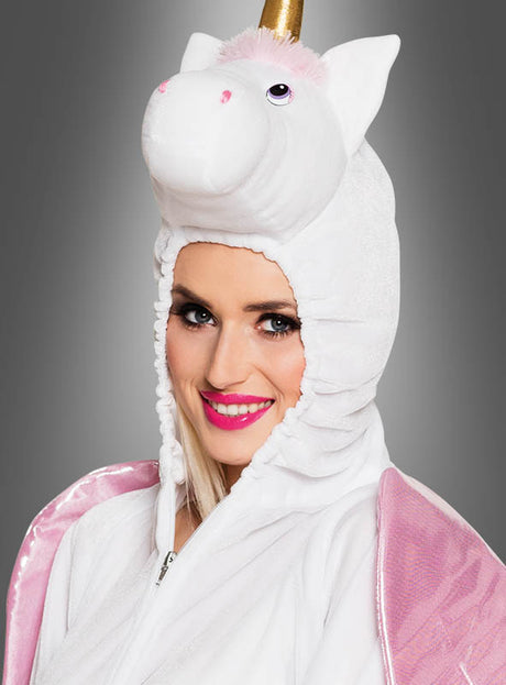 Die Person trägt das „Einhorn-Kostüm für Erwachsene, weiß“ – ein weißes Unisex-Einhornkostüm für Erwachsene mit einer Kapuze in Form eines Einhornkopfes, einem schimmernden goldenen Horn, rosa Innenohren und verspielten rosa Flügeln – und lächelt vor einem grauen Hintergrund in die Kamera. Dieses bezaubernde Unisex-Kostüm eignet sich perfekt für jede Kostümparty.