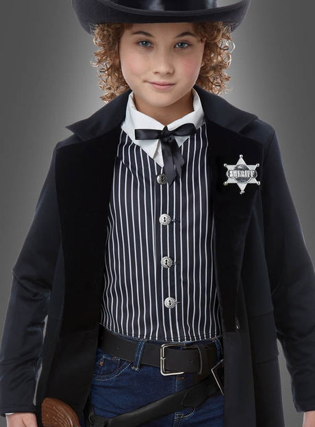 Ein Kind im „Outlaw Sheriff“-Kinderkostüm – bestehend aus einem schwarzen Cowboyhut, einem gestreiften Hemd, einer schwarzen Jacke mit Sheriff-Abzeichen, einer Fliege, einem Gürtel und Jeans – blickt in die Kamera und ist bereit für jede Wild-West-Party.