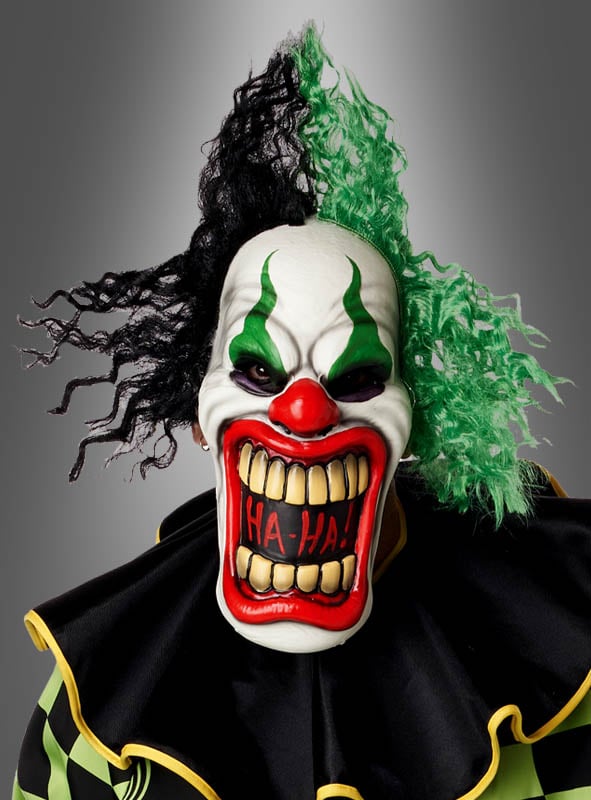 Eine Person, die die gruselige Halloween-Clown-Manni-Maske trägt, die sich durch übertriebene Zähne mit der Aufschrift „HA-HA!“ sowie auffälliges grün-schwarzes Haar auszeichnet. Dieser gruselige Halloween-Clown Manni hebt sich deutlich von einem grauen Hintergrund mit Farbverlauf ab – perfekt für alle, die einen Horrorclown-Look für ihr Halloween-Kostüm suchen.