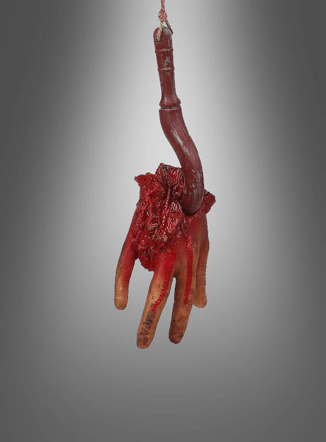 Eine gruselige Halloween-Dekoration mit einem Leichenteil am Haken – eine realistisch aussehende künstliche abgetrennte Hand mit freiliegendem blutigem Gewebe und Knochen, die an einem Seil vor einem schlichten grauen Hintergrund hängt – ist die perfekte gruselige Dekoration, um den Schrecken eines furchterregenden Leichenteils am Haken heraufzubeschwören.