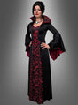Vor einem grauen Hintergrund steht eine Frau, die das Kleid „Vampir Königin Mina Damen“ trägt – ein langes schwarz-rotes Kleid im Gothic-Stil mit ausgestellten Ärmeln und hohem Kragen.