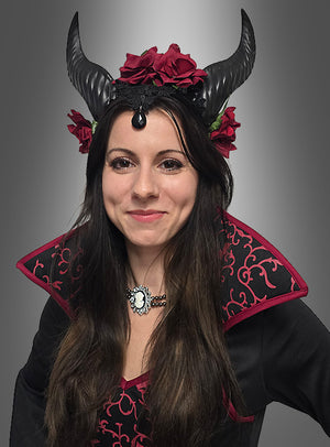 Diese Frau, verkleidet als Vampir-Königin Mina, trägt ein schwarzes Kostüm mit roten Akzenten, kombiniert mit einem Kopfschmuck mit Hörnern und einem Blumenkranz, und steht vor einem grauen Hintergrund – eine atemberaubende Wahl für jedes Halloween-Kostüm für Damen oder perfekt als Vampir-Königin-Kostüm für Damen.