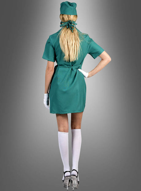 Eine Person in einem kurzen grünen OP-Schwester-Kostüm (Wickelkleid), weißen Handschuhen, weißen Kniestrümpfen und durchsichtigen High Heels steht mit dem Rücken zur Kamera vor einem grauen Hintergrund.