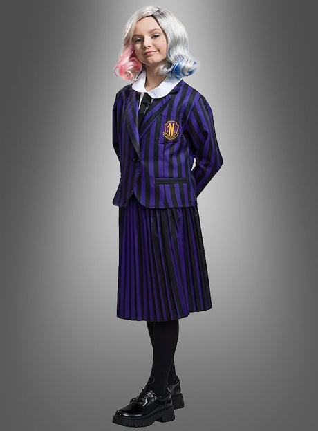 Eine Person, gekleidet in die Schuluniform „Enid Mädchen“ in Schwarz und Lila – mit violetten und schwarzen Streifen sowie einem Wappen –, kombiniert mit schwarzen Schuhen und einer Perücke in Weiß-, Rosa- und Blautönen, die von Enid inspiriert ist, steht vor einem grauen Hintergrund und verkörpert damit perfekt den unverwechselbaren Stil der Nevermore Academy.