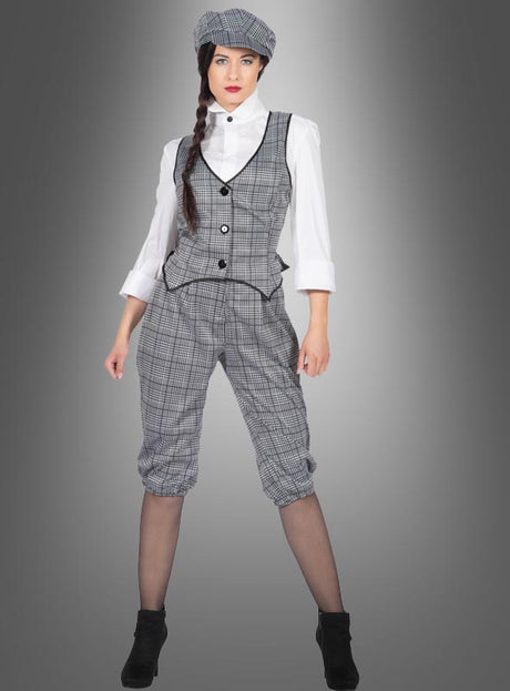 Eine Frau im „20er-Kostüm Outfit Damen Lizzie“ – einer schicken grauen karierten Weste und einem dazu passenden kurzen Knickerbocker-Strumpfhosen-Set, kombiniert mit einer weißen Bluse, einer Baskenmütze und schwarzen Stiefeletten – steht vor einem grauen Hintergrund mit Farbverlauf und präsentiert einen auffälligen, von den 1920er Jahren inspirierten Look.