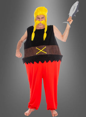 Eine Person im Verleihnix-Kostüm aus „Asterix“ – mit gelber Perücke, falschem Schnurrbart, roter Hose und einem Fisch in der Hand – steht barfuß vor einem grauen Hintergrund und spielt damit spielerisch auf die klassischen „Asterix“-Comic-Kostüme an.