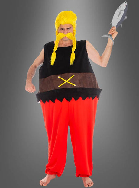 Eine Person im Verleihnix-Kostüm aus „Asterix“ – mit gelber Perücke, falschem Schnurrbart, roter Hose und einem Fisch in der Hand – steht barfuß vor einem grauen Hintergrund und spielt damit spielerisch auf die klassischen „Asterix“-Comic-Kostüme an.