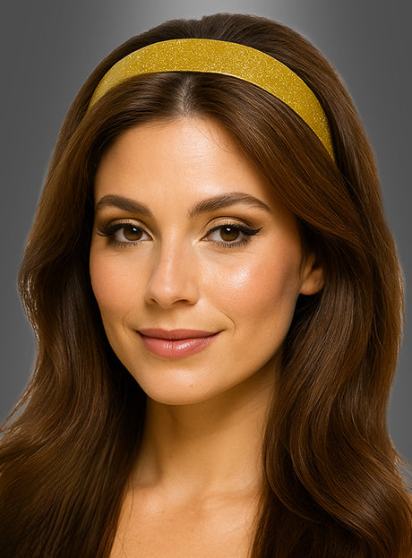 Eine Frau mit langen braunen Haaren trägt das goldene Glitzer-Haarband „Disco Glitzer“, dazu ein dezentes Make-up und ein leichtes Lächeln, vor einem grauen Hintergrund.