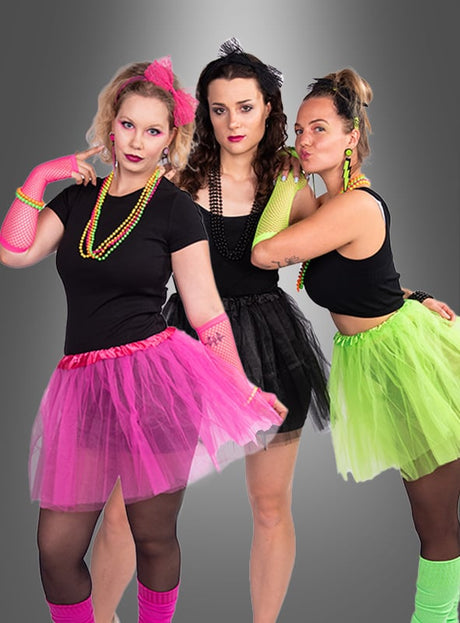 Drei Frauen posieren vor einem grauen Hintergrund mit Farbverlauf und präsentieren farbenfrohe, von den 1980er Jahren inspirierte Outfits, darunter das 80er-Jahre-Kostüm-Set mit Tüllrock – komplett mit Tüllröcken, Netzhandschuhen, neonfarbenen 80er-Jahre-Accessoires und schwarzen Oberteilen – eine perfekte Inspirationsquelle für Ihre nächste 80er-Jahre-Mottoparty oder zum Zusammenstellen eines authentischen 80er-Jahre-Kostüms für Damen.