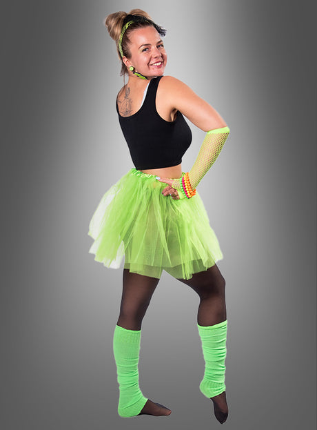 Eine lächelnde Person posiert vor einem grauen Hintergrund mit Farbverlauf und trägt das 80er-Jahre-Kostüm-Set mit Tüllrock – bestehend aus einem schwarzen Crop-Top, einem neongrünen Tutu, Stulpen und einem Netzhandschuh. Dieses Ensemble ist die perfekte Inspiration für Ihre nächste 80er-Jahre-Mottoparty oder einen authentischen 80er-Jahre-Kostüm-Look für Damen mit klassischen 80er-Jahre-Accessoires für das echte Retro-Feeling.