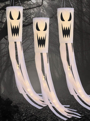 Drei Geist-Windsäcke mit Geistermotiv als Halloween-Gartendekoration mit LED-Beleuchtung, verziert mit schwarzen, grimmigen Gesichtern und langen weißen Bändern, hängen in einer nebligen, dunklen Waldkulisse und sorgen so für eine unheimliche Halloween-Atmosphäre. Diese LED-Windsäcke eignen sich perfekt als Halloween-Akzente in der Gartendekoration, um Ihrem Außenbereich einen gruseligen Touch zu verleihen.