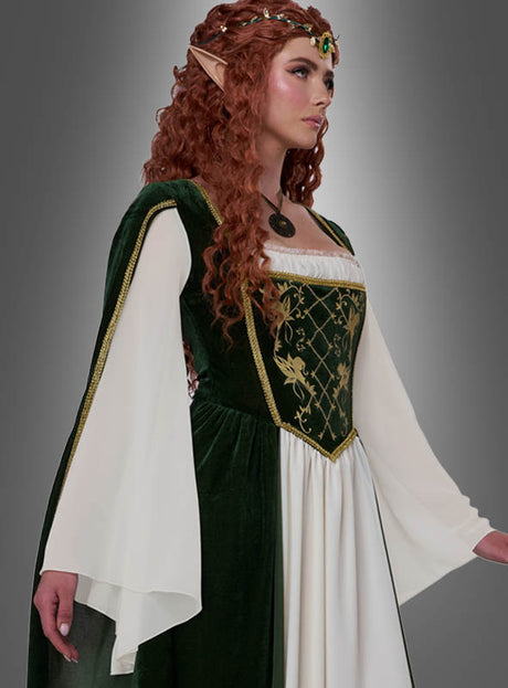 Eine Frau in einem grün-weißen, mittelalterlich anmutenden Kleid mit langen Ärmeln – einem exquisiten „Elfenkönigin Emerald“-Damenkostüm – trägt eine Halskette, einen mit Edelsteinen besetzten Kopfschmuck und spitze Elfenohren, während sie vor einem grauen Hintergrund mit Farbverlauf steht. Dieses elegante Fantasy-Kostüm eignet sich perfekt, um sich in eine Elfenkönigin zu verwandeln.