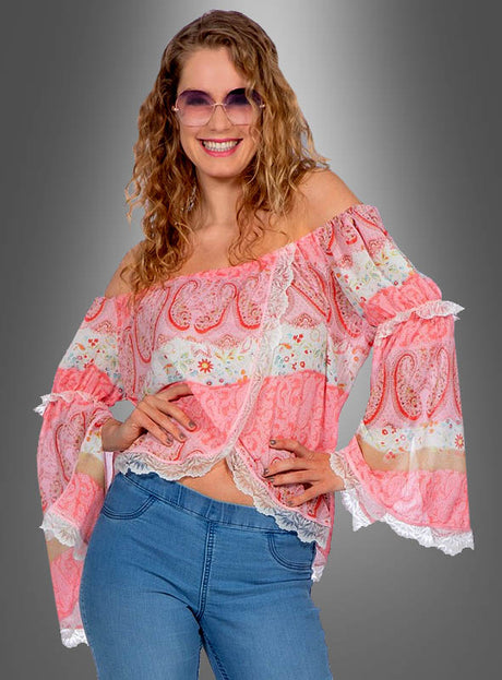 Diese Frau trägt die „Luftige Paisley-Bluse im Boho-Stil“ mit ihrem luftigen, schulterfreien Schnitt und den ausgestellten Ärmeln und kombiniert das Oberteil mit einer blauen Jeans. Vor einem grauen Hintergrund mit Farbverlauf lächelt sie selbstbewusst – und verkörpert damit mühelosen Boho-Chic.