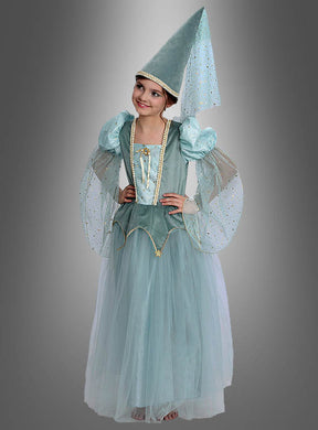 Ein Kind, das das „Traumhaftes Prinzessin Kleid Adelia Kinderkostüm“ trägt – ein hellblaues Märchenkostüm im mittelalterlichen Stil mit Puffärmeln, einem langen Tüllrock und einem hohen, spitzen Hut, der mit einem wallenden Schleier verziert ist –, steht vor einem grauen Hintergrund.