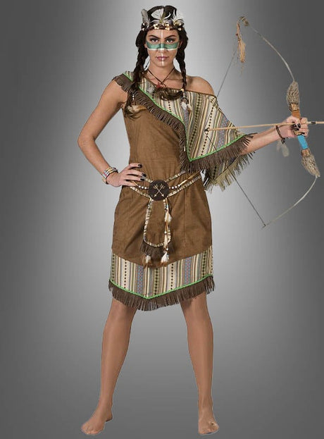 Eine Frau in einem „Indianer-Kostüm“ von Silbermond Damen, das von der Kleidung der amerikanischen Ureinwohner inspiriert ist, hält Pfeil und Bogen in der Hand, während sie barfuß vor einem grauen Hintergrund mit Farbverlauf steht.