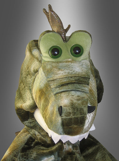 Ein Kind im „Dinosaurier-Kostüm für Kinder“ – ein grüner Anzug mit großen Augen, weißen Zähnen und strukturiertem Stoff – posiert vor einem grauen Hintergrund mit Farbverlauf.