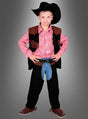Ein kleiner Junge im Cowboy-John-Kinderkostüm – mit schwarzem Hut, rotem Karohemd, schwarzer Weste, Chaps und braunen Schuhen – steht mit den Händen in die Hüften gestemmt vor einem grauen Hintergrund mit Farbverlauf.