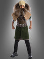 Ein Kind, das das Dwalin-Kinderkostüm aus „Der Hobbit“ trägt – darunter einen großen Kunstbart, eine braune Weste, eine grüne Tunika, schwarze Stiefel und ein gelb gemustertes Stirnband –, steht mit angewinkelten Armen und geballten Fäusten da.