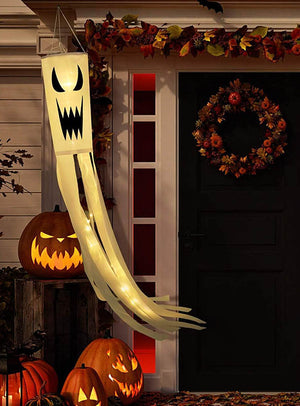 Ein „Geist“-Windsack als Halloween-Gartendekoration mit LED, der neben einer schwarzen Tür leuchtet, die mit einem Herbstkranz geschmückt und von geschnitzten Kürbislaternen und Herbstblättern umgeben ist, sorgt für die perfekte gruselige Verandadekoration.