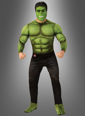 Eine Person, die das grüne „Hulk Muskelkostüm Endgame für Erwachsene“-Superheldenkostüm trägt, komplett mit passender Gesichtsbemalung, steht mit geballten Fäusten vor einem grauen Hintergrund.