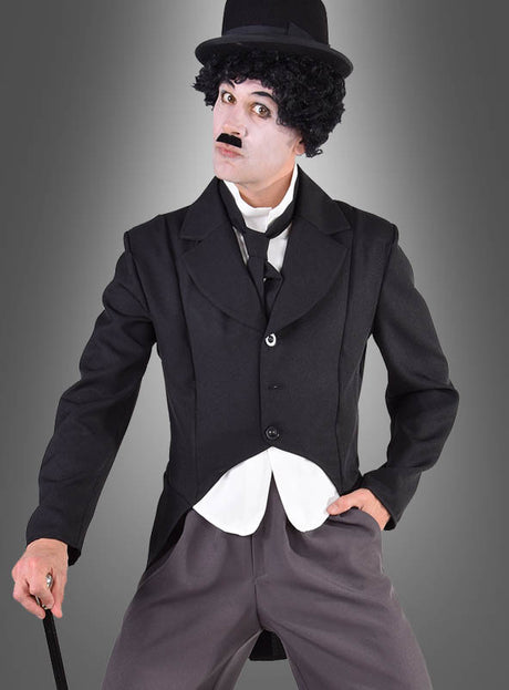 Eine Person, die das „Charlie Komiker“-Kostüm im Frack-Stil trägt – ein klassisches, von Charlie Chaplin inspiriertes Ensemble bestehend aus einem schwarzen Anzug, einer Melone, einem Spazierstock, einem aufgemalten Schnurrbart und weißer Gesichtsbemalung –, steht vor einem grauen Hintergrund; eine ideale Wahl für den Karneval für Herren oder alle, die ein Kostüm einer ikonischen Figur aus dem Stummfilm suchen.