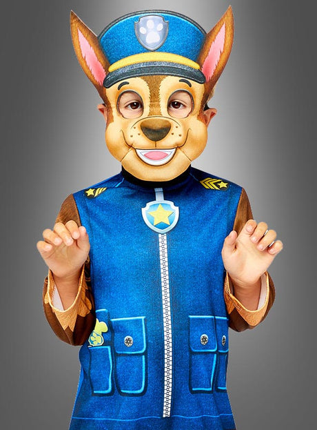 Ein Kind, das das Chase-Kostüm aus „Paw Patrol“ mit Maske trägt – bestehend aus einem blauen Outfit und einer Maske mit Hundeohren –, steht vor einem einfarbigen grauen Hintergrund.