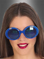 Eine Person mit glattem braunem Haar trägt eine große, runde blaue Brille im Retro-Look der 60er Jahre und roten Lippenstift und lächelt vor einem grauen Hintergrund mit Farbverlauf.