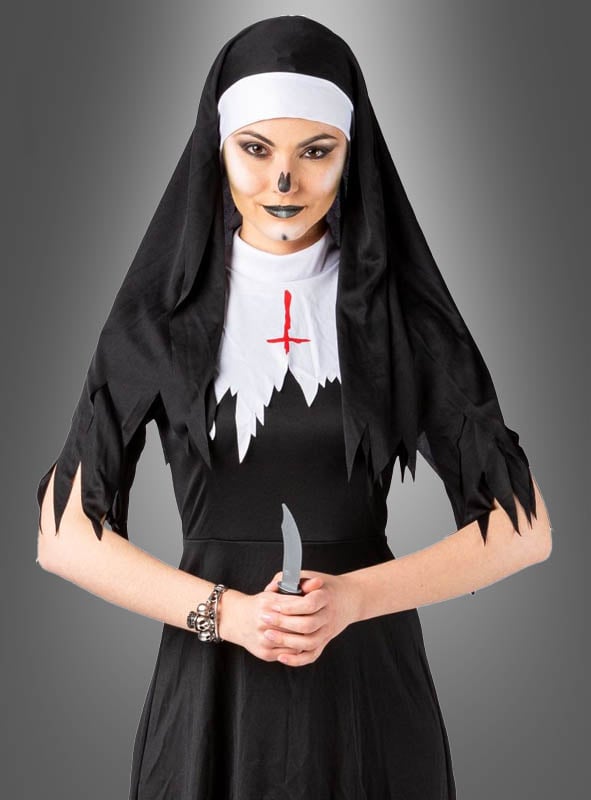 Eine Person im Halloween-Nonnen-Damenkostüm – mit zerfetztem schwarzem Stoff, weißen Akzenten und einem Make-up, das an einen Totenschädel erinnert – hält ein Messer in der Hand und steht vor einem grauen Hintergrund, was ihr den ultimativen gruseligen Klosterfrauen-Look verleiht.