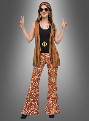 Eine Person, die das Hippie-Komplettkostüm „Earth Love“ trägt – bestehend aus einer von den 1970er Jahren inspirierten Fransenweste, einer gemusterten Flower-Power-Schlaghose, einer Halskette mit Peace-Zeichen, einer Sonnenbrille und einem Stirnband –, steht da und zeigt mit beiden Händen das Peace-Zeichen.