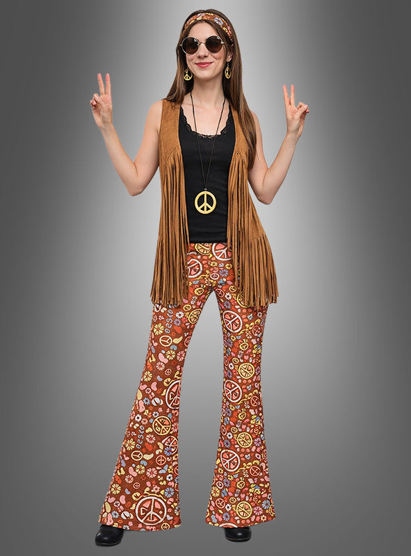 Eine Person, die das Hippie-Komplettkostüm „Earth Love“ trägt – bestehend aus einer von den 1970er Jahren inspirierten Fransenweste, einer gemusterten Flower-Power-Schlaghose, einer Halskette mit Peace-Zeichen, einer Sonnenbrille und einem Stirnband –, steht da und zeigt mit beiden Händen das Peace-Zeichen.