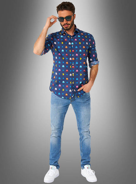 Ein Mann in einem „Pac-Man“-Hemd von OppoSuits im Retro-Stil einer 80er-Jahre-Mottoparty, hellblauen Jeans und weißen Sneakers, der eine Sonnenbrille trägt und vor einem grauen Hintergrund mit Farbverlauf posiert.