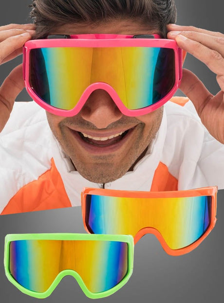 Eine Person lächelt, während sie eine Skibrille „Karneval Neon“ mit verspiegelter Scheibe und rosa Rahmen trägt – damit ist sie die perfekte, verspielte Neon-Partybrille oder das ideale Accessoire für jede Karnevalsveranstaltung. Zwei weitere „Skibrille Karneval Neon“-Brillen, eine in Orange und eine in Grün, sind unten auf grauem Hintergrund abgebildet und präsentieren sich als farbenfrohe Après-Ski-Accessoires für jeden festlichen Anlass.