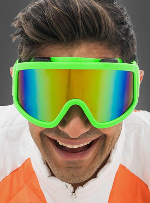 Eine Person in einer weiß-orangefarbenen Jacke und einer großen grünen Skibrille „Karneval Neon“ mit regenbogenfarbenen Gläsern, die vor einem grauen Hintergrund in die Kamera lächelt – ein ideales Après-Ski-Accessoire, um bei jeder Winterfeier aufzufallen.