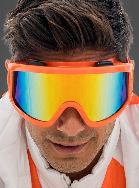 Ein Mann mit einer Skibrille „Karneval Neon“ – einer reflektierenden orangefarbenen Skibrille, die sich ideal als auffälliges Après-Ski-Accessoire oder als markantes Statement für „Skibrille Karneval“ eignet – und einer weißen Jacke mit orangefarbenen Akzenten, der vor einem schlichten grauen Hintergrund nach vorne blickt.