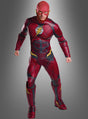 Eine Person in einem roten Superheldenkostüm mit einem gelben Blitz-Emblem steht mit geballten Fäusten vor einem grauen Hintergrund und bringt damit den ikonischen Stil des „Deluxe Flash Herrenkostüms“ aus der Justice League perfekt zur Geltung.