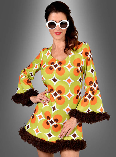 Eine Frau trägt das „70er Retrokleid Damen grün-braun“ – ein Retro-Kleid mit grünem, orangefarbenem und gelbem Muster sowie braunen Verzierungen –, dazu eine weiße Sonnenbrille, und posiert vor einem Hintergrund mit Farbverlauf. Dies ist die perfekte Wahl für jede Mottoparty oder eine Feier im Vintage-Stil.